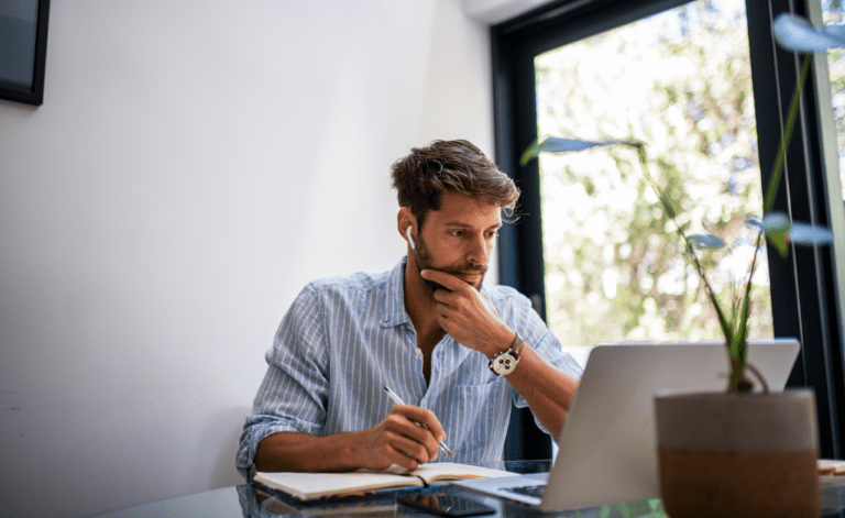 Professional taking notes while researching GRC platform options on a laptop at a home office desk